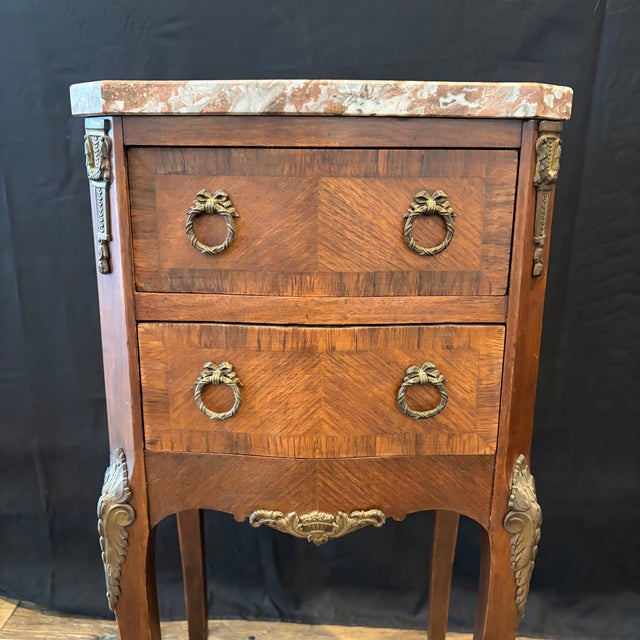 A refined pair of French marble top side tables, bedside tables, or nightstands, crafted in richly figured walnut with...
