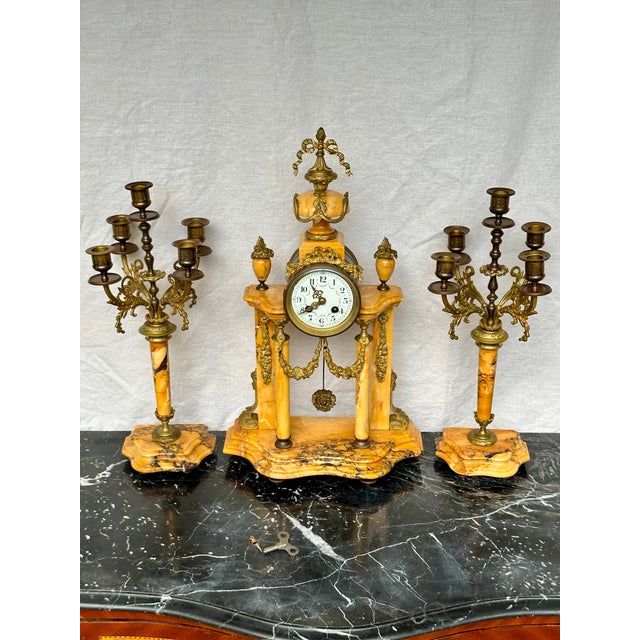 Presenting a breathtaking late 19th-century French Louis XVI-style mantel clock garniture set, crafted from peachy ochre-...