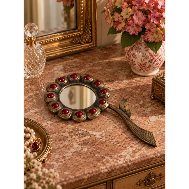A charming vintage hand mirror crafted from substantial cast brass, featuring an Art Nouveau-inspired floral silhouette...