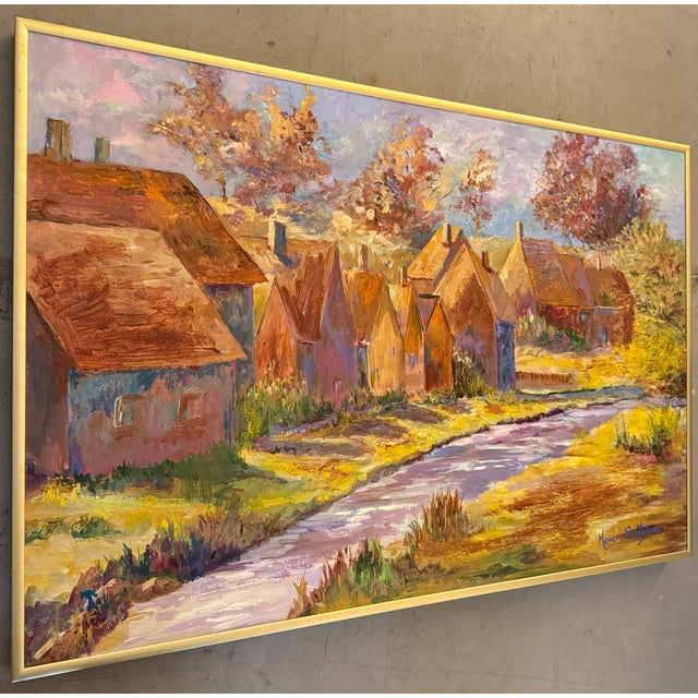 This artwork is a framed impressionistic painting of a rural village landscape with a small river. The painting appears is...