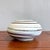 This low, rounded vessel features a creamy glaze accented by hand-drawn brown rings that spiral organically around its...