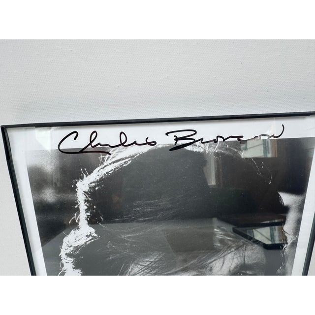 Framed black-and-white portrait of Charles Bronson, signed prominently in black ink across the upper border. A strong...