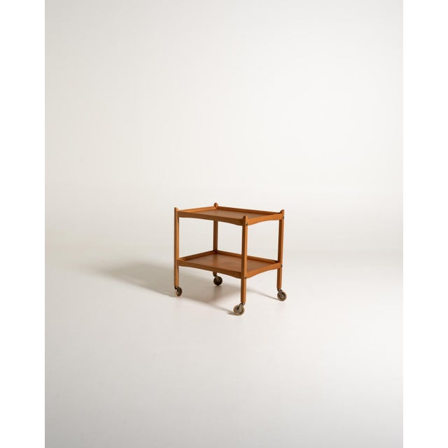 Scandinavian 1960s oak serving trolley with raised-edge shelves, curved crosspieces, and exposed metal screws....