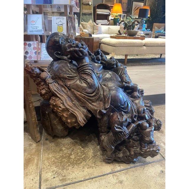 Impressive large-scale carved wooden Laughing Buddha surrounded by playful children, symbolizing joy and abundance....