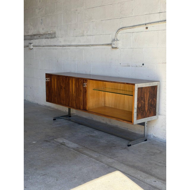 An architectural low-slung credenza configuration features sliding cabinet doors that glide smoothly to reveal integrated...