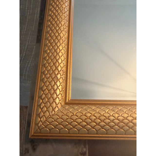 Elegant rectangular wooden wall mirror featuring an antiqued gold frame with an allover fish scale texture pattern. The...