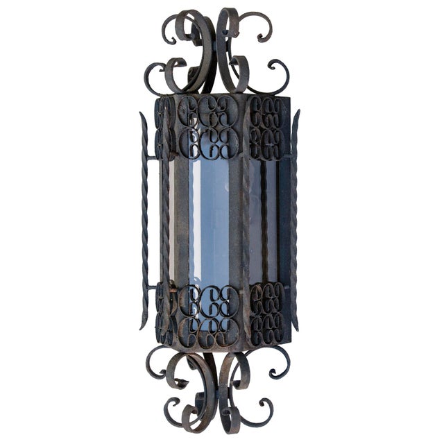 Spanish Revival or Gothic-style hand-forged wrought iron lantern pendant. It features ornate scrollwork with a dark gray...