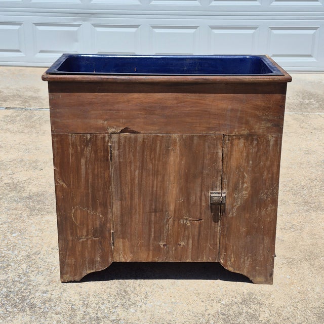 This is an antique American primitive dry sink made of distressed brown painted pine wood and fitted with a cobalt blue...
