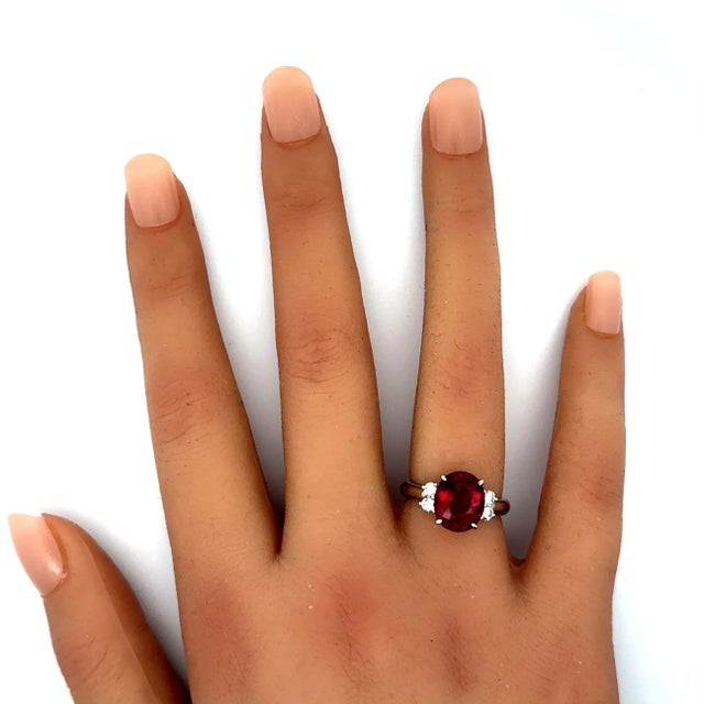 A contemporary ring featuring a 3.2 carat rubellite with an oval cut. The rubellite displays a vivid red color, exuding...
