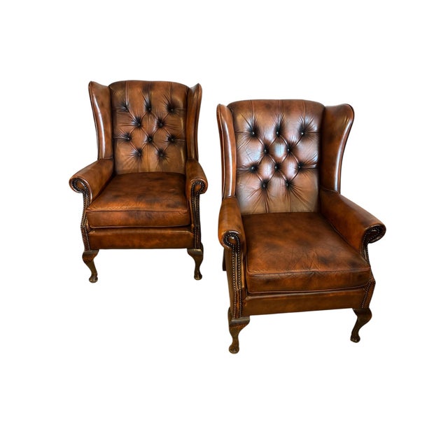 A handsome pair of vintage English wingback armchairs in cognac-brown leather with deep-button tufting and nailhead trim....