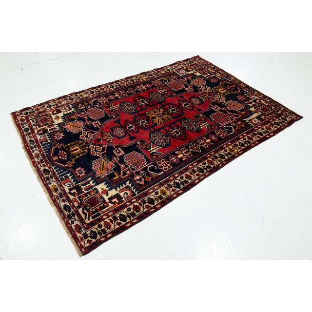 This vintage malayer handknotted Persian wool rug has a red field with dark blue, beige, and yellow accents. This rug...