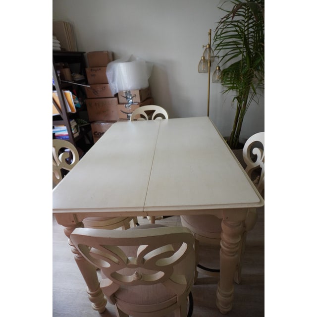 Large white solid wood pedestal dining table with extension leaf and upholstered scroll-back seating. The table converts...