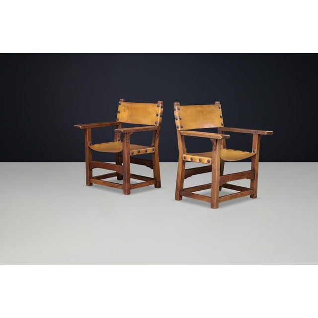 Striking pair of Spanish armchairs crafted in solid beechwood with original patinated cognac leather seat and back panels,...