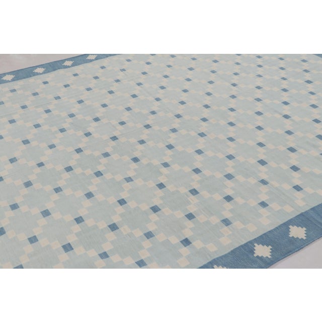 This 8x10 Dhurrie rug features a sophisticated geometric mosaic in shades of blue and cream, representing an exciting...