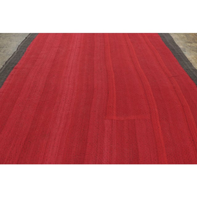 This 9x11 vintage kilim flatweave, handwoven in wool circa 1950–1959, features a rich solid red field framed by a charcoal...