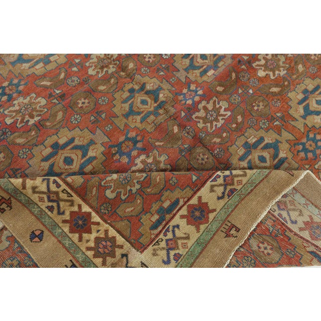 A hand-knotted wool Persian Bakshaish rug dating back to circa 1900. The main field features repetitive rows of stylized...