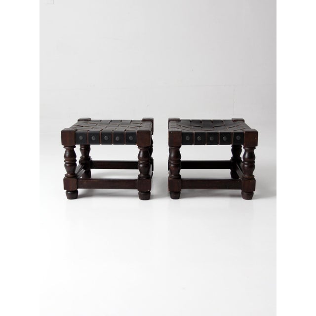 This matching pair of stools features handwoven leather strap seats set within dark-stained wood frames, showcasing...
