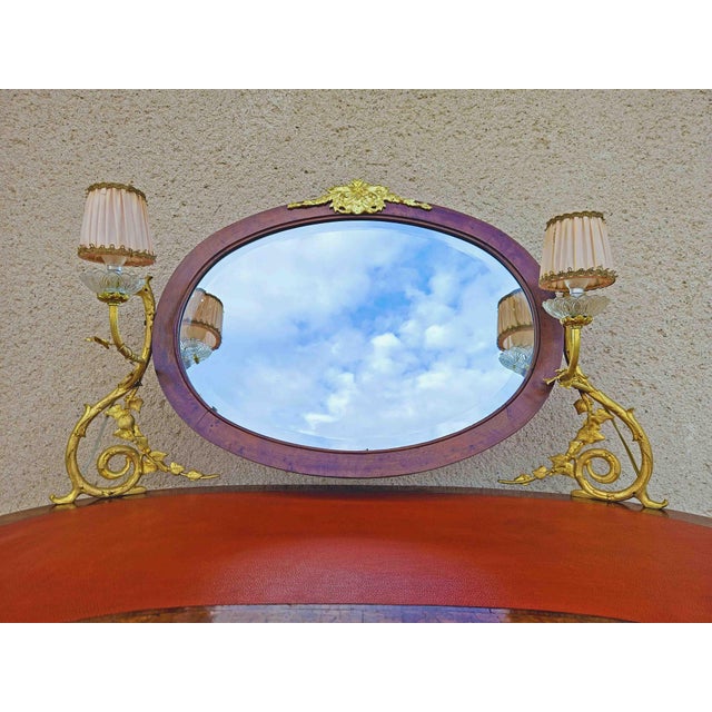 Kidney-shaped dressing table, with leather top, marquetry and rosewood fillets. The beveled mirror supported by a gilded...