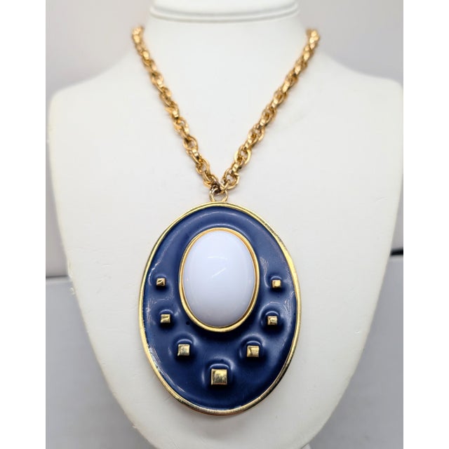 Modernist goldtone oval pendant with matte navy enamel and white cabochon rhinestone with raised goldtone squares on a...