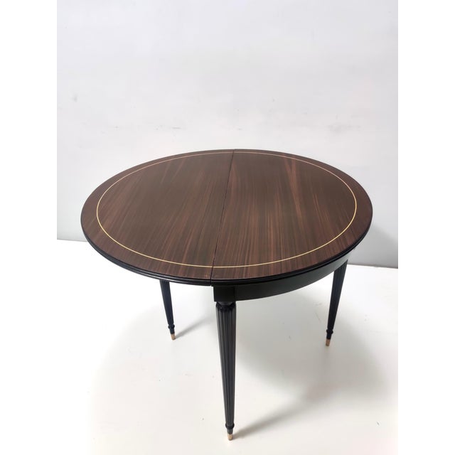 Made in Italy, 1960s. It features an ebonized beech and black walnut frame with brass feet caps. This round folding table...