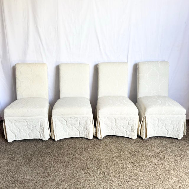 Elegant set of four vintage Regency Parsons dining chairs, each fully skirted in a soft white damask fabric. The timeless...