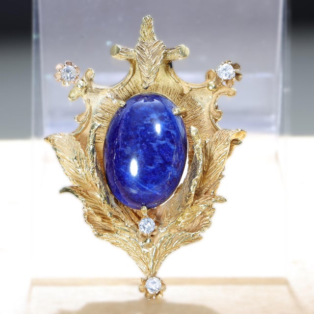 Circa 1940s 18K yellow gold brooch pendant featuring a large oval cabochon lapis lazuli set within a sculptural botanical...