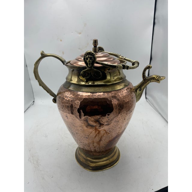 Hammered copper ewer with brass details, including a spout in the form of a fish head, ornate scale handle, and lid...