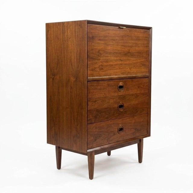 This Mid-Century Modern secretary desk features a rich, warm wood grain finish resting on tapered legs. The top section...