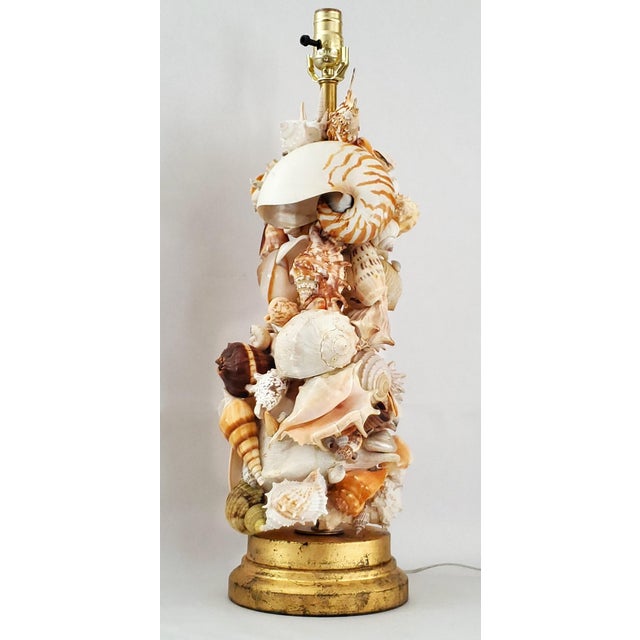 Offering an extra-large vintage seashell table lamp with distressed gold leafed base and seashell finial, circa 1950s....