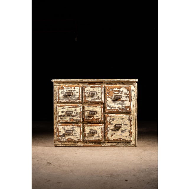 This 8-drawer apothecary cabinet features chipping white paint over exposed natural wood. Each of these drawers features...