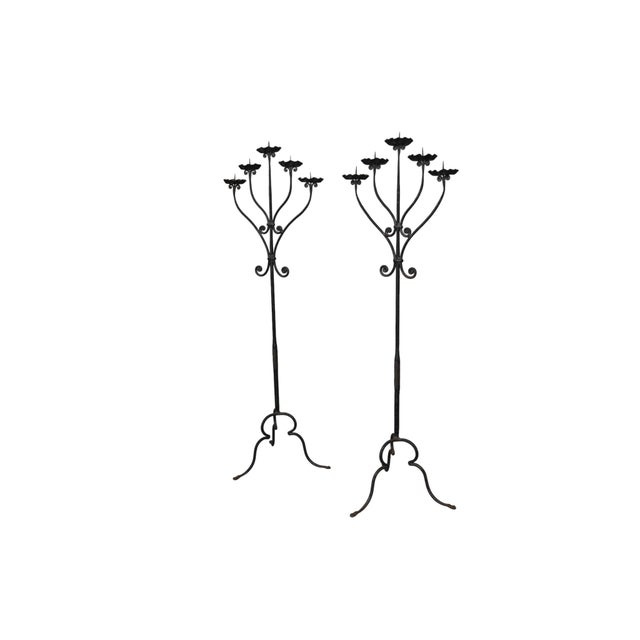 A pair of Renaissance Revival wrought iron five candle floor candelabra. Scrolled arms support ribbon shaped drip pans...