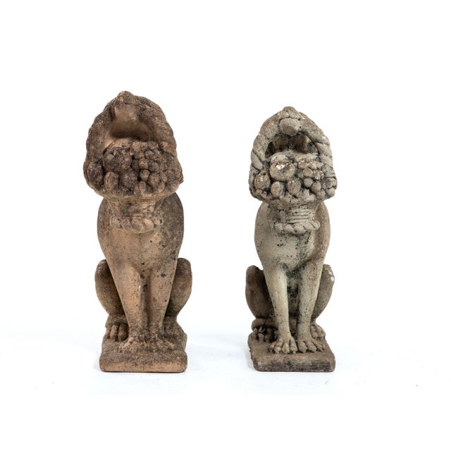 A matched pair of English mid-20th-century composite stone dogs sit upright on square bases, each holding a molded fruit...