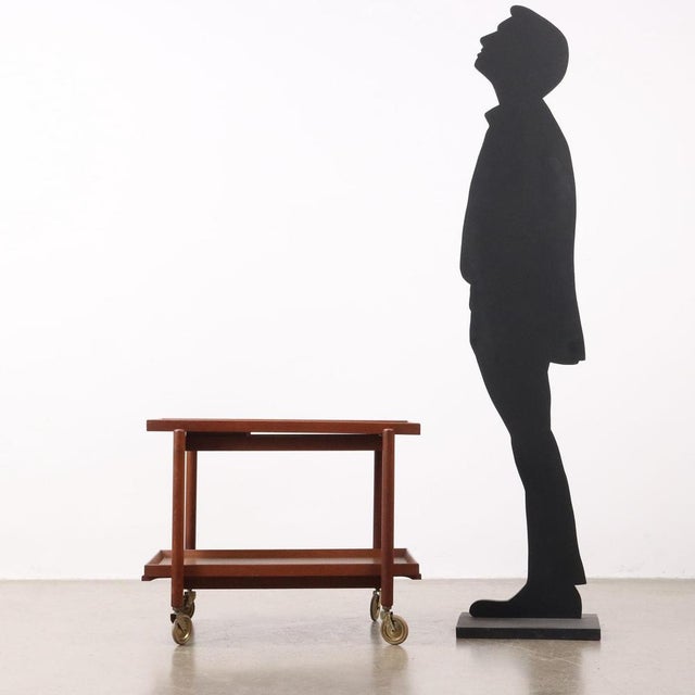 Service trolley with upper shelf sliding on the side and removable lower shelf. In teak wood. This piece is attributed to...