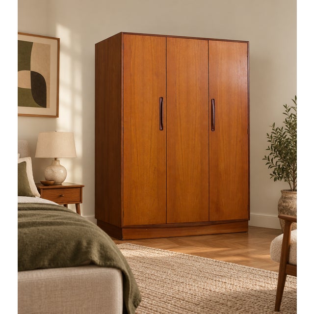 A stylish mid-century G Plan Fresco triple wardrobe in warm teak, featuring three clean-fronted doors, contrasting darker...