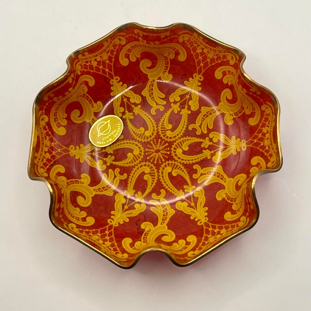 A ruffle edged glass bowl decorated in an intricate flourishing design on a red background with a starburst center and...