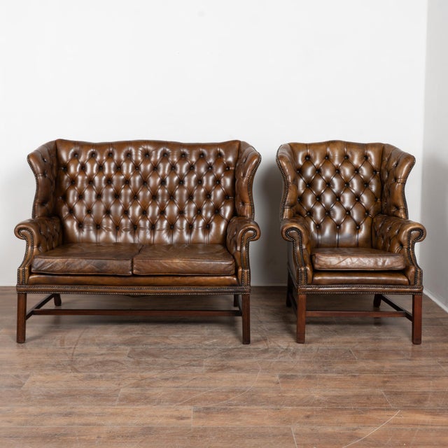 Vintage Chesterfield loveseat and matching club chair upholstered in rich brown leather with tufted button backs, wingback...
