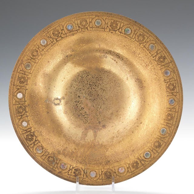 Round shallow flared bowl on a short foot, mottled d'ore finish, embossed border with geometric and floral design accented...