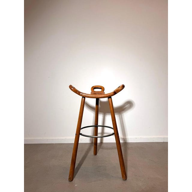 Sculptural Marbella bar stool , featuring the characteristic curved saddle seat with integrated handles and elegant...