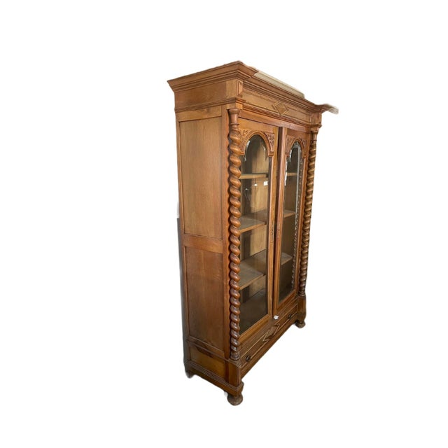 Tall wooden display chest that has two glass doors, 2 bottom drawers, and 2 spiral columns. The style is art deco between...