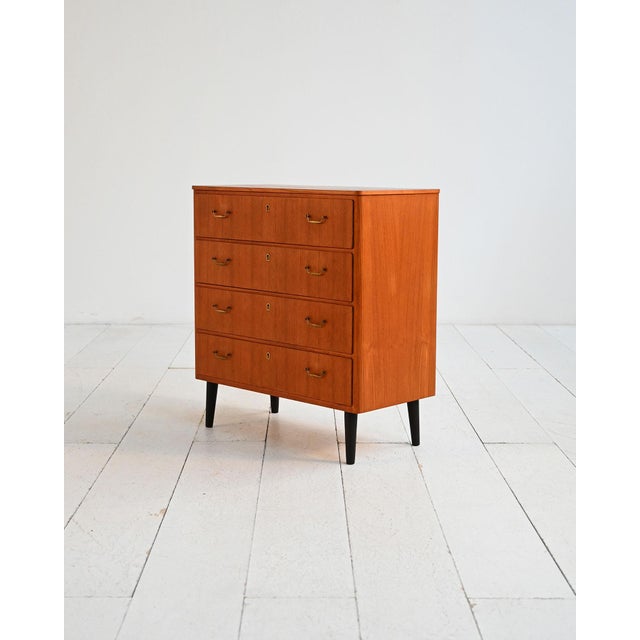 Teak chest of drawers with four front drawers, brass handles and keyholes, and turned legs painted black. Scandinavian...