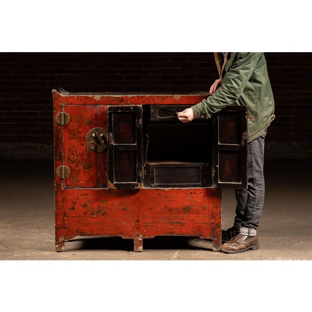 Small-scale cabinet in traditional Chinese form, finished in a timeworn red lacquer with hand-painted decorative scenes...