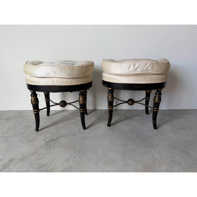 Striking and elegant, this pair of vintage Hollywood Regency ottomans showcases a bold black and gold ebonized finish...
