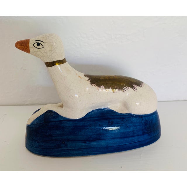 A vintage Staffordshire figural inkwell shaped like a resting greyhound or whippet on a blue pillow with gold trim. The...