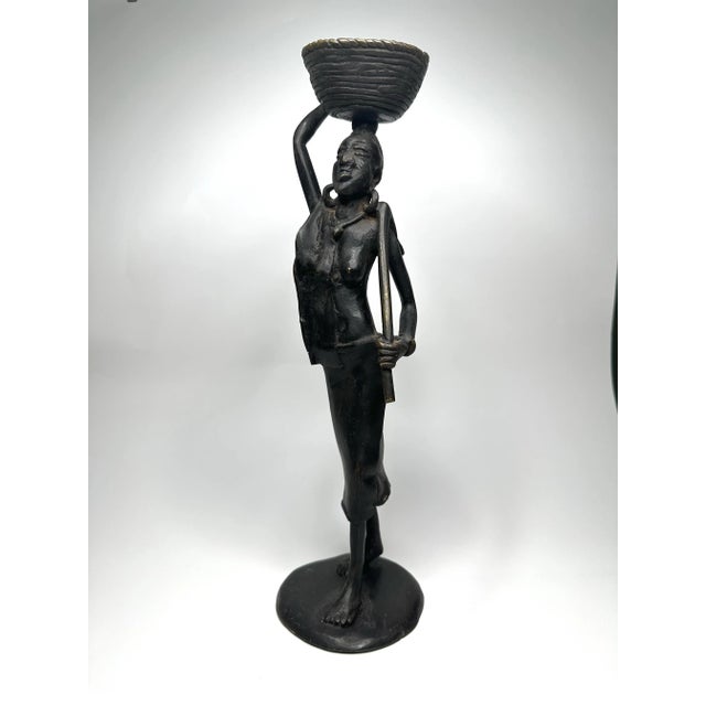 The beautiful bronze like patina of this figurine enhances the details. The African woman is carrying a basket and a...