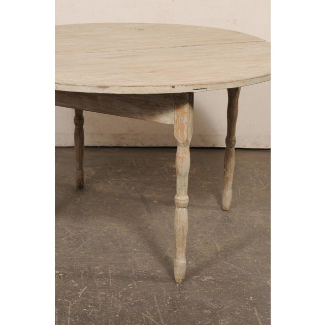 A Swedish painted wood round table, with drop leaf that converts to demi-lune, from the 19th century. This antique table...