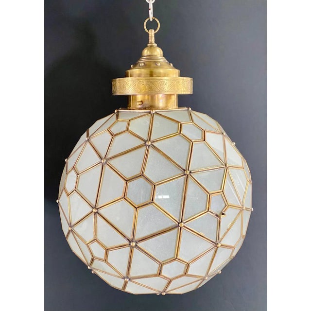 A striking Art Deco-style globe pendant featuring an intricate geometric leaded-glass design. Panels of opaque white milk...
