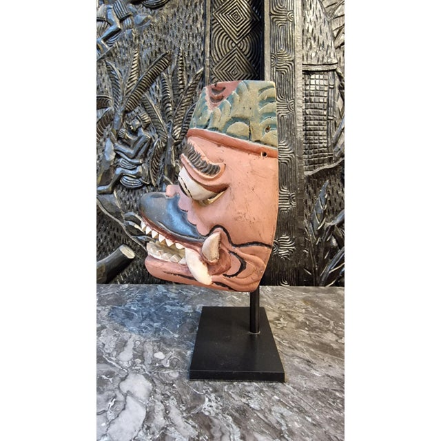 Polychrome Balinese mask on a base. This mask, with its fierce and exaggerated features, is carved from Diya Kaduru wood...