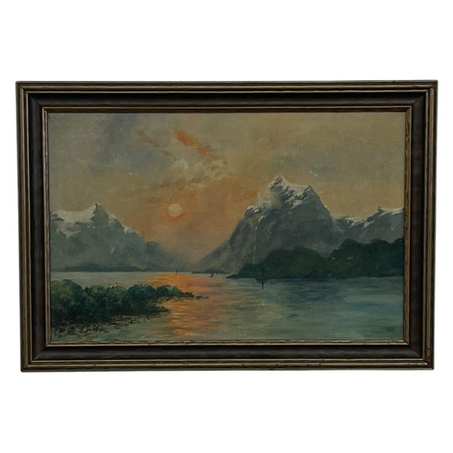 Vintage framed landscape painting depicting a tranquil mountain at sunset with snow-capped peaks, calm water, and a warm...