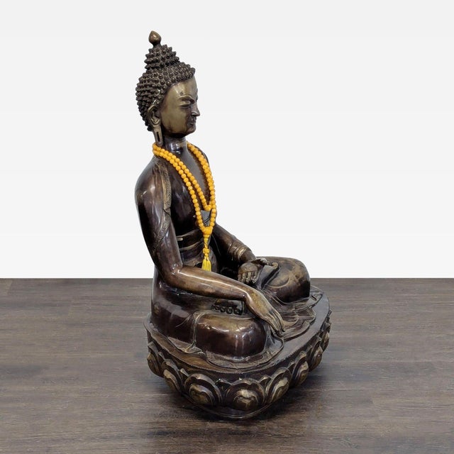 This elegant antique bronze sculpture from India features a seated Buddha with fine details, including a textured hair...