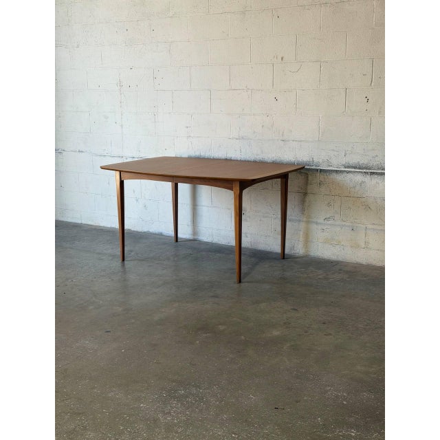 This minimalist dining table features a clean rectangular silhouette with gracefully tapered legs. The fixed top...